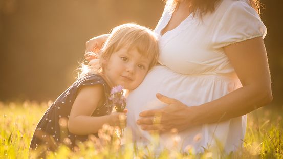 Das Bild zeigt ein Kind, das am Bauch einer schwangeren Mutter horcht.